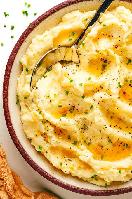 Creamy brown butter mashed potatoes in a white serving bowl topped with melted butter and chives.