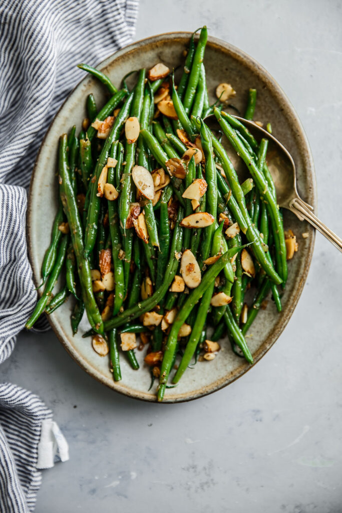 Green beans tossed with toasted almonds and lemon zest served on a neutral serving dish