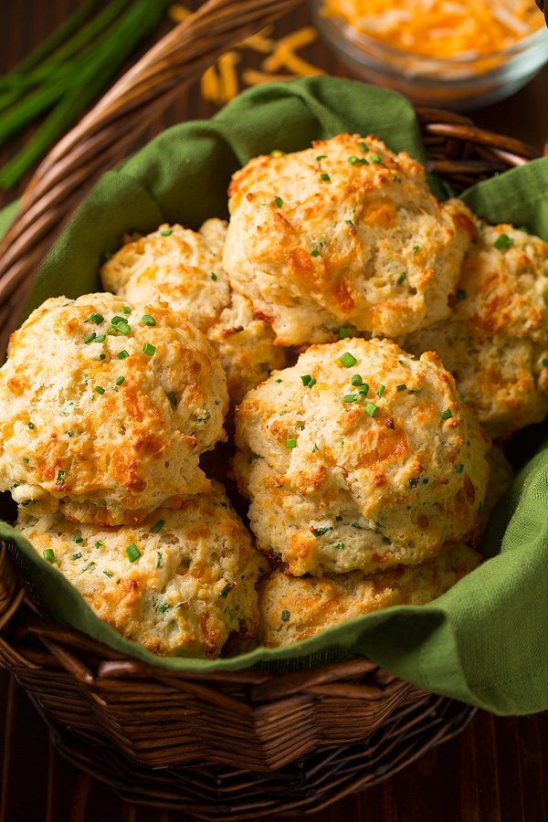 Freshly baked cheddar chive biscuits stacked in a woven basket