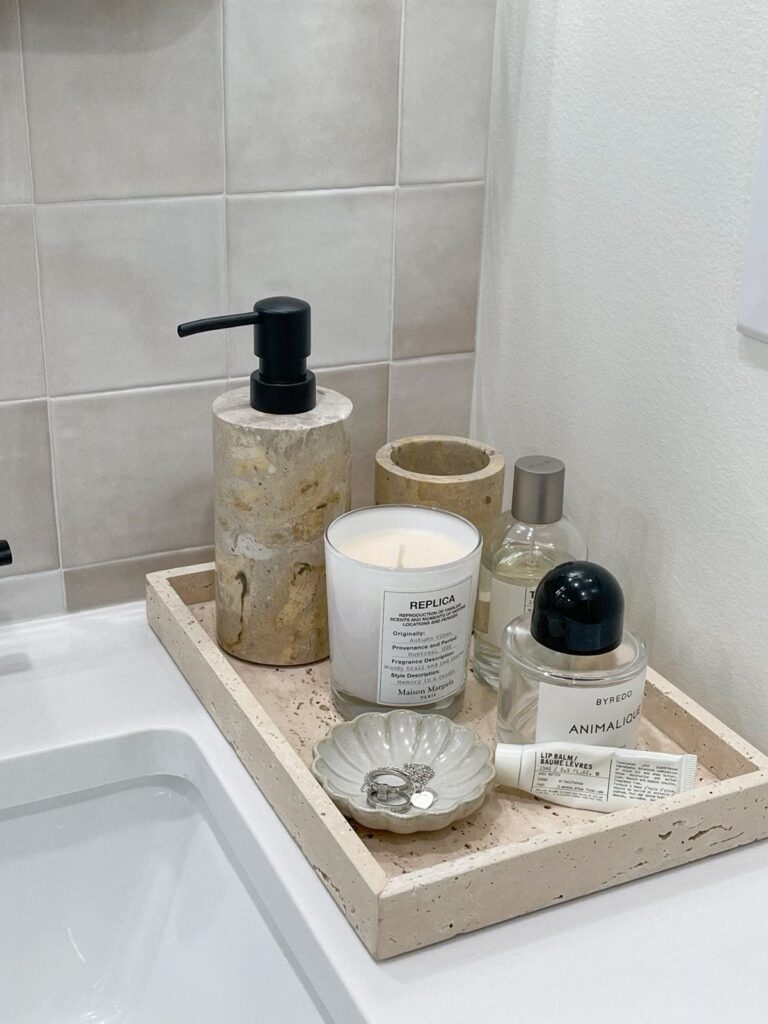 Bathroom counter styled with a marble tray holding a soap dispenser, perfume, a candle, and jewelry dish