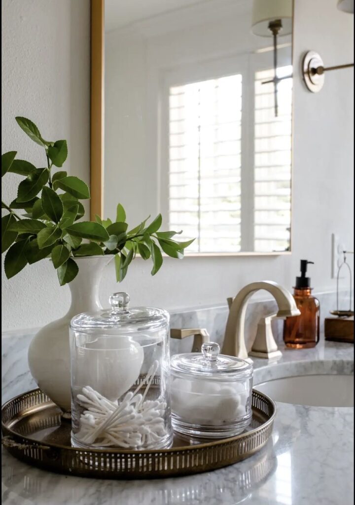 Glass jar holding cotton rounds styled on a bathroom counter